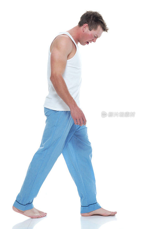 全长/侧视图20-29岁英俊的人/短发白人男性/年轻男子走在白色背景穿着睡衣/背心谁是打哈欠/疲倦/情绪压力